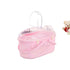 Pink baby booties in a clear plastic bag on a light wooden floor with decorative items.
